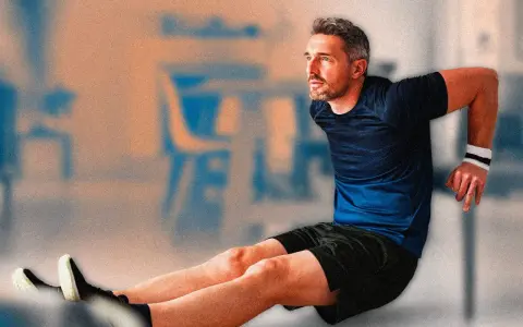 Uomo con polsino bianco esegue allenamento con sedia, piegando le braccia. Gambe tese in avanti, scarpe sportive.