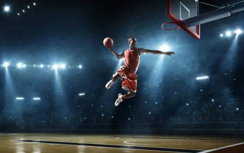 Un giocatore di basket in aria, con la palla in mano, dimostra la sua forza muscolare con un salto spettacolare sotto le luci dell'arena.