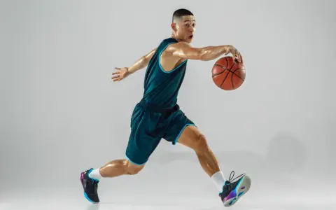 Giovane giocatore di basket in azione, con la palla in mano. La sua postura dinamica è il risultato di allenamenti e test posturali mirati.