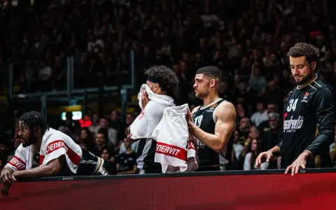Giocatori di basket in panchina, asciugandosi il sudore con asciugamani. Un promemoria che anche gli atleti hanno bisogno di recupero e proteine in un giorno intenso.