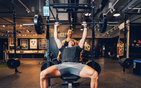 Uomo solleva bilanciere con donna che lo osserva, allenamento che stimola diversi tipi di fibre muscolari.
