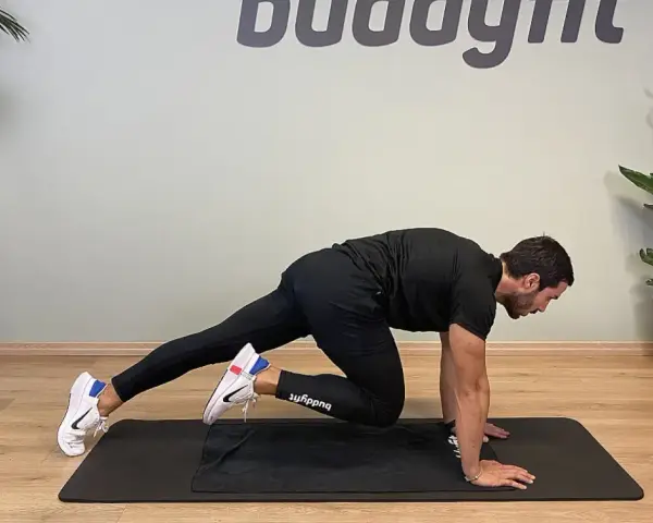 Uomo in posizione di plank, porta un ginocchio al petto, simulando un esercizio di montagna scalatore per un allenamento completo.