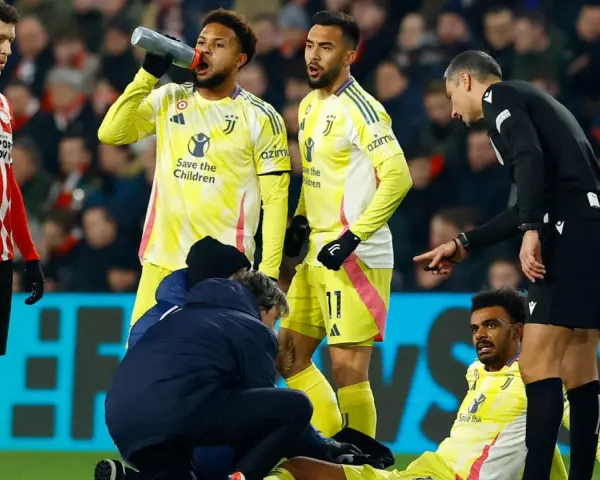 Giocatori di calcio in campo, uno è a terra, assistito dallo staff medico. L'arbitro osserva attentamente, preoccupato per i possibili infortuni nel calcio.