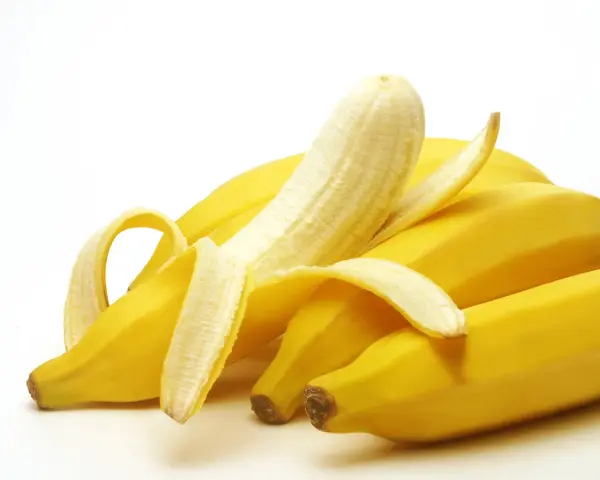 Un grappolo di banane gialle, una parzialmente sbucciata, che fa pensare a quanto potassio contiene una banana.