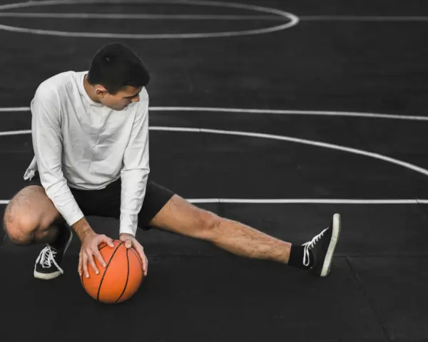 Giovane atleta si allunga sul campo da basket, con una palla arancione. Il suo corpo mostra la necessità di riposo muscolare 48 ore.