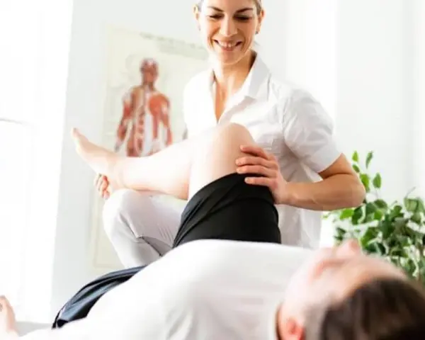 Un fisioterapista esegue un trattamento alla gamba di un paziente, con un poster anatomico sullo sfondo.