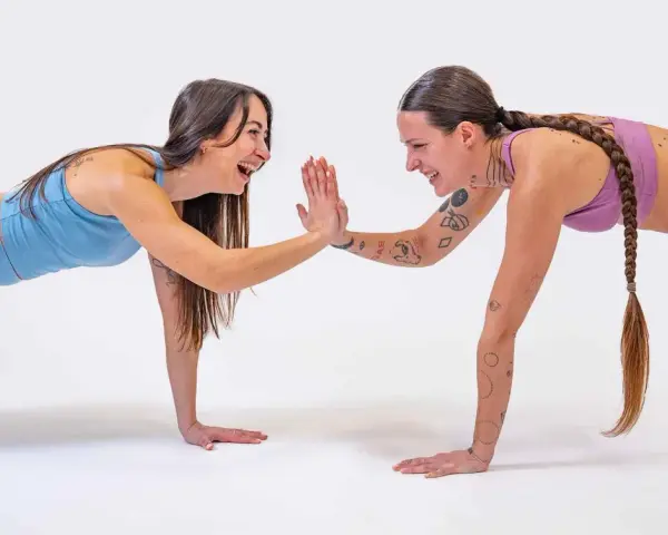 Due donne in posizione di plank si danno il cinque, un allenamento post parto che rafforza il corpo e lo spirito.
