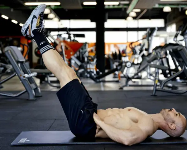 Uomo muscoloso esegue reverse crunch su panca in palestra, concentrato sull'allenamento addominale.