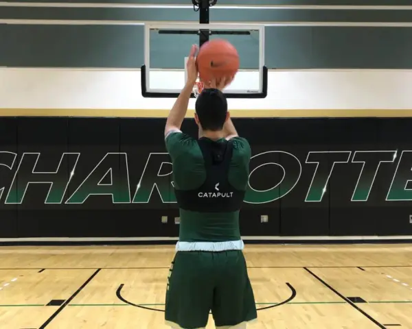 Basketball player in green uniform shooting a basketball in a gym with "CHARLOTTE" logo on the wall.