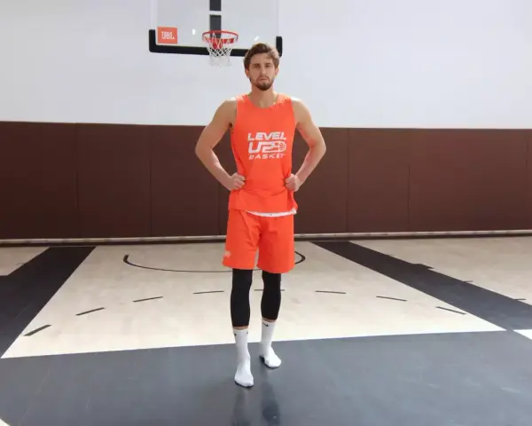 Giovane giocatore di basket in tenuta arancione, pronto per esercizi per i piedi sul campo.