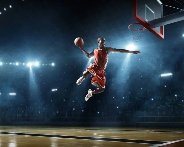 Un giocatore di basket in aria, con la palla in mano, dimostra la sua forza muscolare con un salto spettacolare sotto le luci dell'arena.