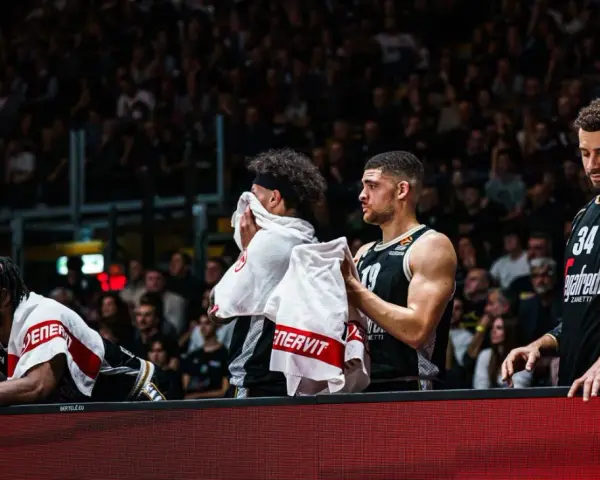 Giocatori di basket in panchina, asciugandosi il sudore con asciugamani. Un promemoria che anche gli atleti hanno bisogno di recupero e proteine in un giorno intenso.