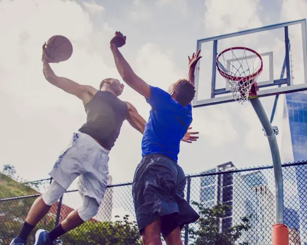 Due giocatori di basket saltano per un canestro. L'energia che li spinge, come i carboidrati complessi quali sono, è visibile in ogni movimento.