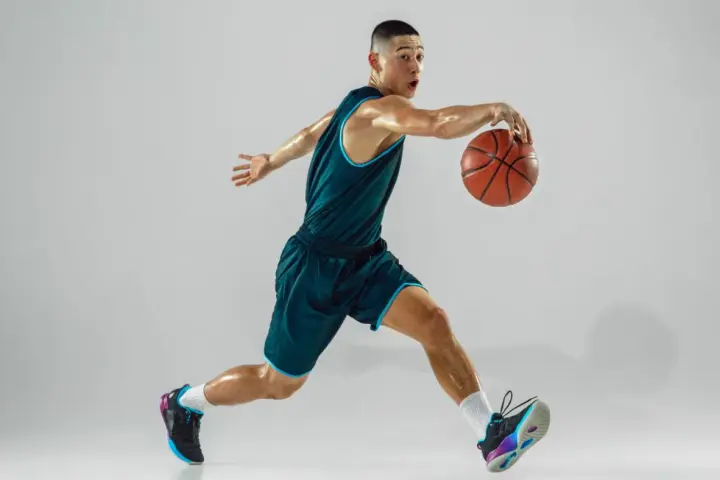 Giovane giocatore di basket in azione, con la palla in mano. La sua postura dinamica è il risultato di allenamenti e test posturali mirati.