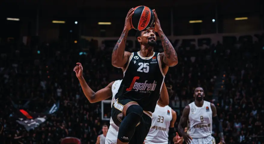 Giocatore di basket con la palla in alto, pronto al tiro. La folla sugli spalti è un tripudio di colori, un vero e proprio rapporto calorico di emozioni.