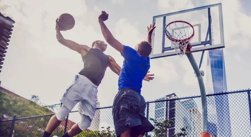 Due giocatori di basket in aria, uno schiaccia la palla, l'altro tenta di bloccarlo. Un perfetto equilibrio energetico in campo.
