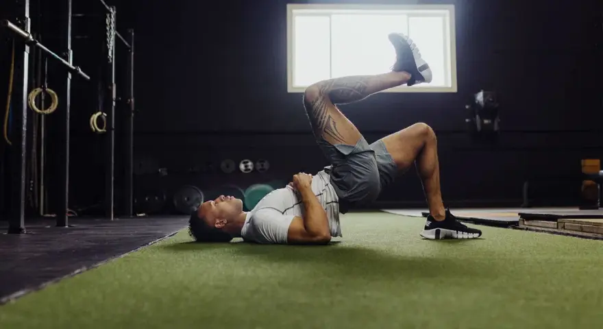Uomo esegue ponte per gamba singola, un esercizio utile per la fisioterapia per ernia del disco, in palestra.