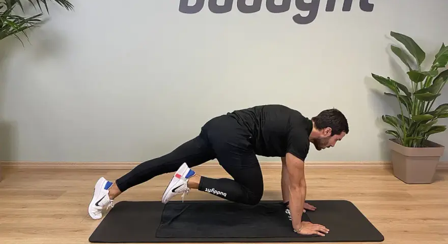 Uomo in posizione di plank, porta un ginocchio al petto, simulando un esercizio di montagna scalatore per un allenamento completo.