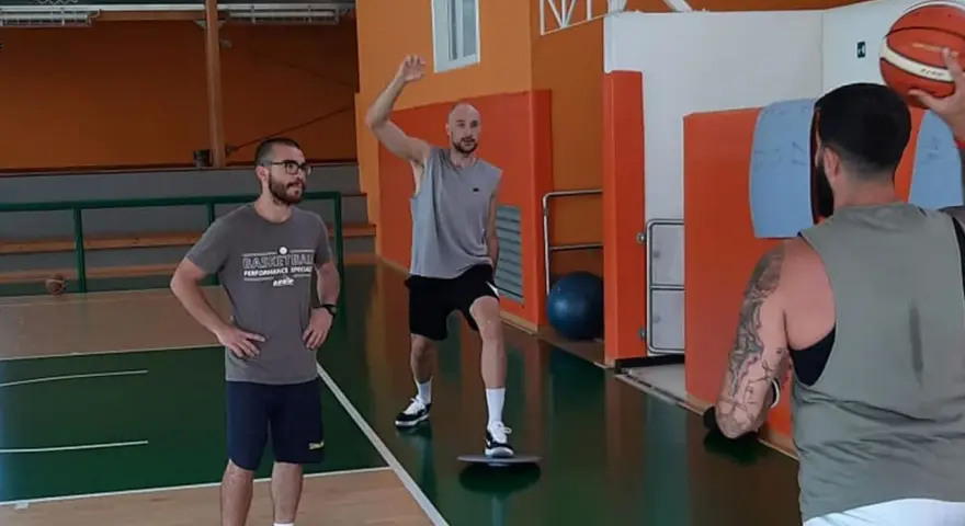 Allenamento in palestra: un uomo esegue torsioni del busto su una tavoletta di equilibrio, mentre un altro lo osserva.