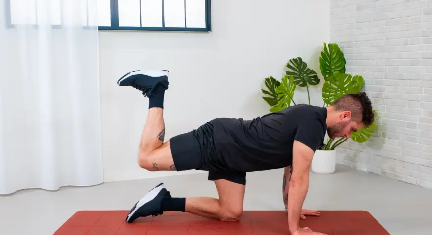 Uomo in posizione a quattro zampe su un tappetino rosso, esegue un esercizio di ginnastica per anca sollevando una gamba piegata.