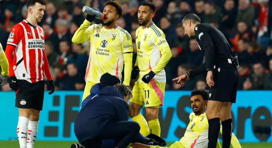 Giocatori di calcio in campo, uno è a terra, assistito dallo staff medico. L'arbitro osserva attentamente, preoccupato per i possibili infortuni nel calcio.