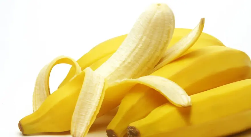 Un grappolo di banane gialle, una parzialmente sbucciata, che fa pensare a quanto potassio contiene una banana.