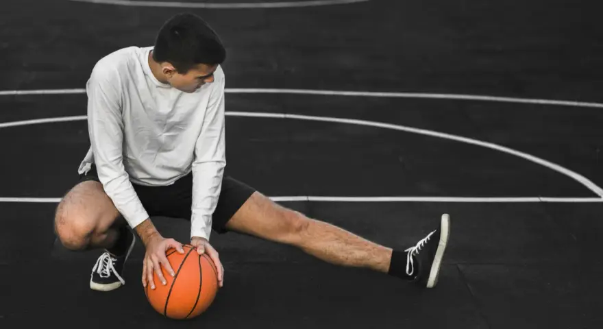 Giovane atleta si allunga sul campo da basket, con una palla arancione. Il suo corpo mostra la necessità di riposo muscolare 48 ore.