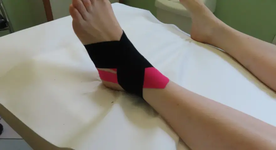 Caviglia fasciata con nastro kinesiologico nero e rosa per supporto.