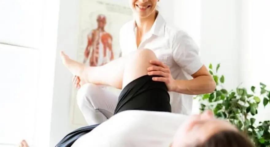 Un fisioterapista esegue un trattamento alla gamba di un paziente, con un poster anatomico sullo sfondo.