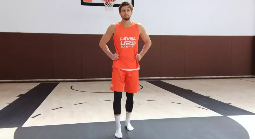 Giocatore di basket in tenuta arancione, mani sui fianchi, con enfasi sui muscoli del bacino laterali.