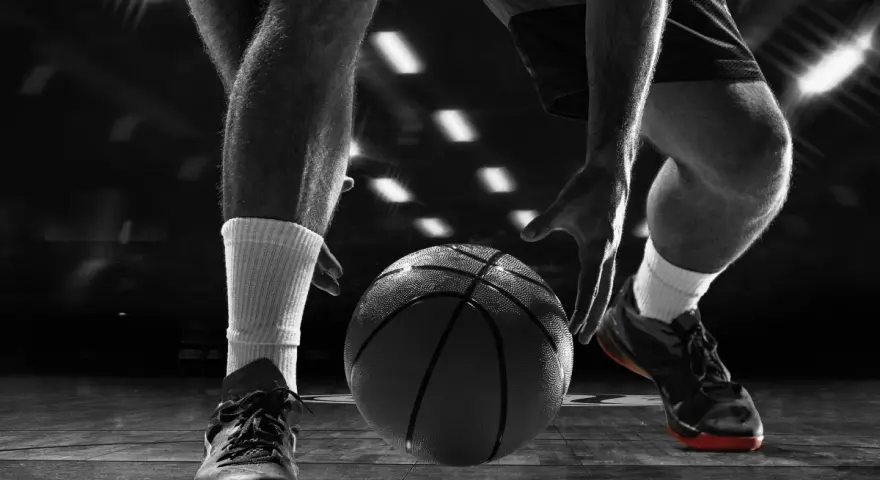 Giocatore di basket in azione, concentrato sul palleggio. Allenarsi per migliorare il fiato è fondamentale per vincere.
