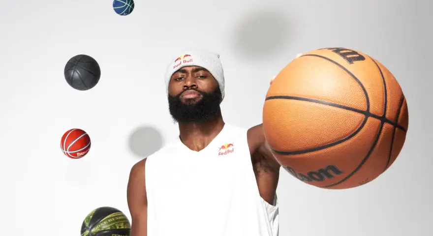 Un giocatore di basket con un berretto Red Bull, circondato da palloni che sembrano fluttuare. Prendi un respiro profondo, inspira ed espira, pronto per il gioco.