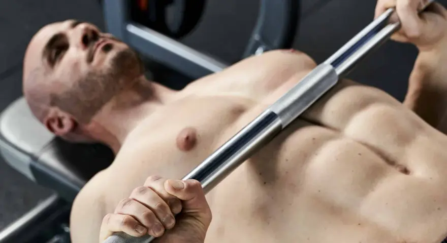 Uomo a petto nudo che solleva un bilanciere, un esempio di allenamento per l'ipertrofia muscolare.