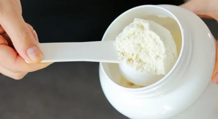 Mano che preleva proteine in polvere da un barattolo bianco con un misurino. Ideale per il recupero post-allenamento.