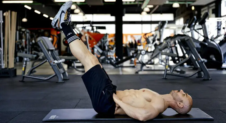 Uomo muscoloso esegue reverse crunch su panca in palestra, concentrato sull'allenamento addominale.