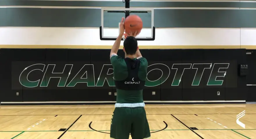 Basketball player in green uniform shooting a basketball in a gym with "CHARLOTTE" logo on the wall.