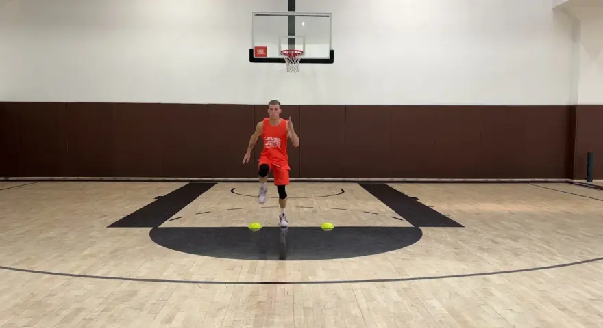 Giovane atleta in divisa arancione esegue uno degli **10 esercizi di riscaldamento** su un campo da basket, con coni gialli a terra.