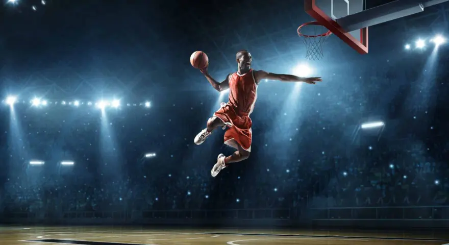 Un giocatore di basket in aria, con la palla in mano, dimostra la sua forza muscolare con un salto spettacolare sotto le luci dell'arena.