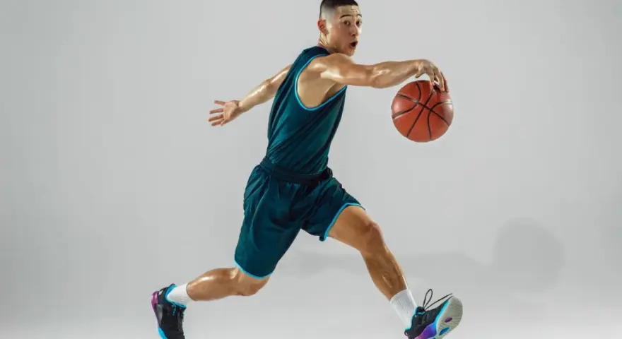 Giovane giocatore di basket in azione, con la palla in mano. La sua postura dinamica è il risultato di allenamenti e test posturali mirati.