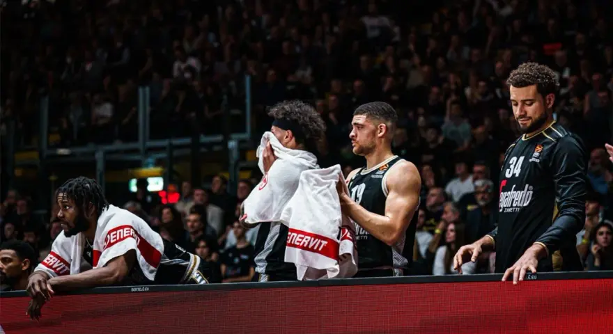 Giocatori di basket in panchina, asciugandosi il sudore con asciugamani. Un promemoria che anche gli atleti hanno bisogno di recupero e proteine in un giorno intenso.