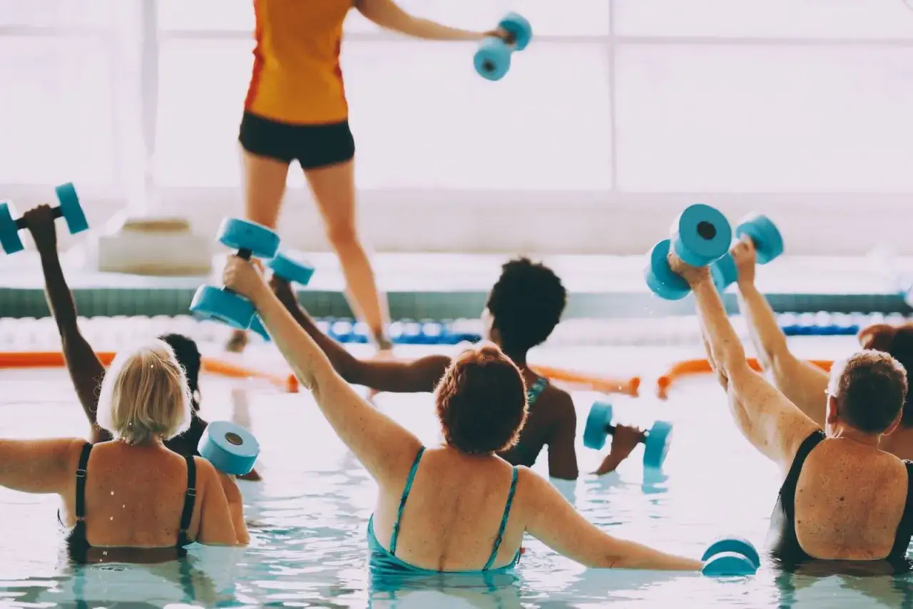 Donne in piscina praticano acquagym con pesi blu. Scopri i benefici e le controindicazioni di questa attivit&agrave; acquatica.