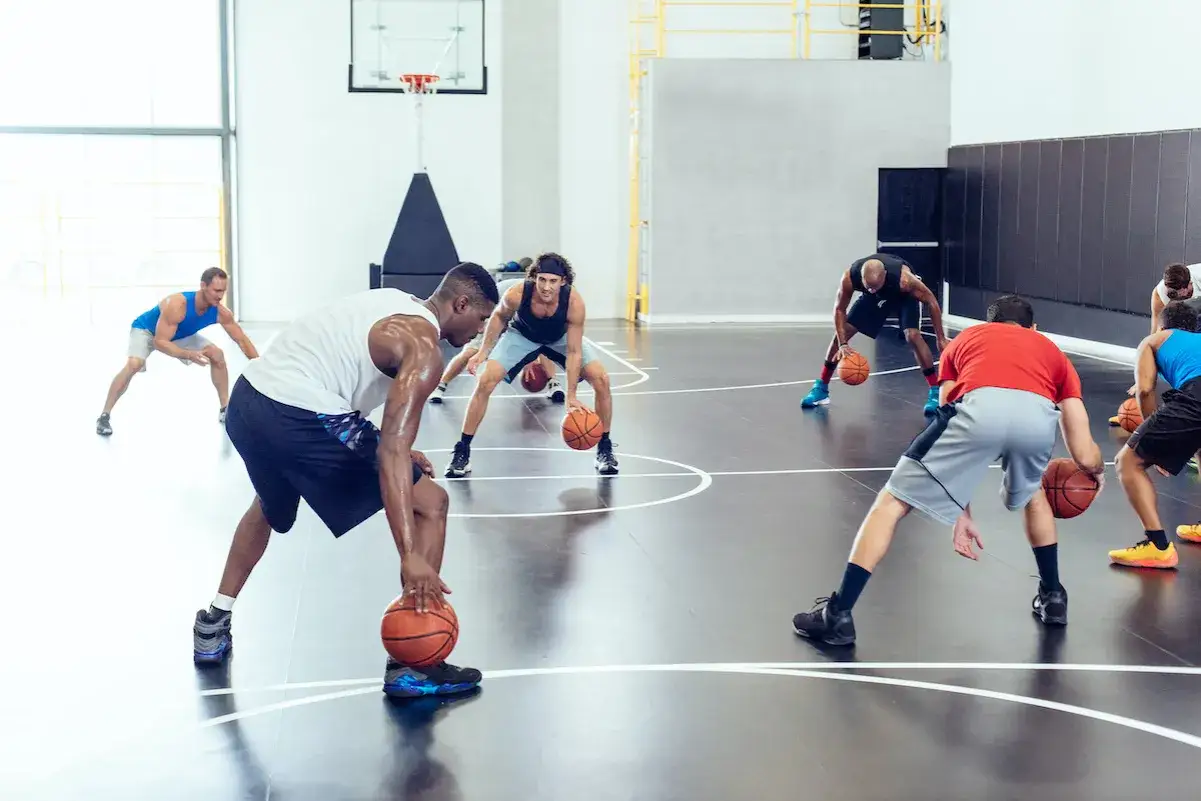 Giocatori di basket eseguono 10 esercizi di riscaldamento con la palla in palestra, concentrati e in posizione di difesa.