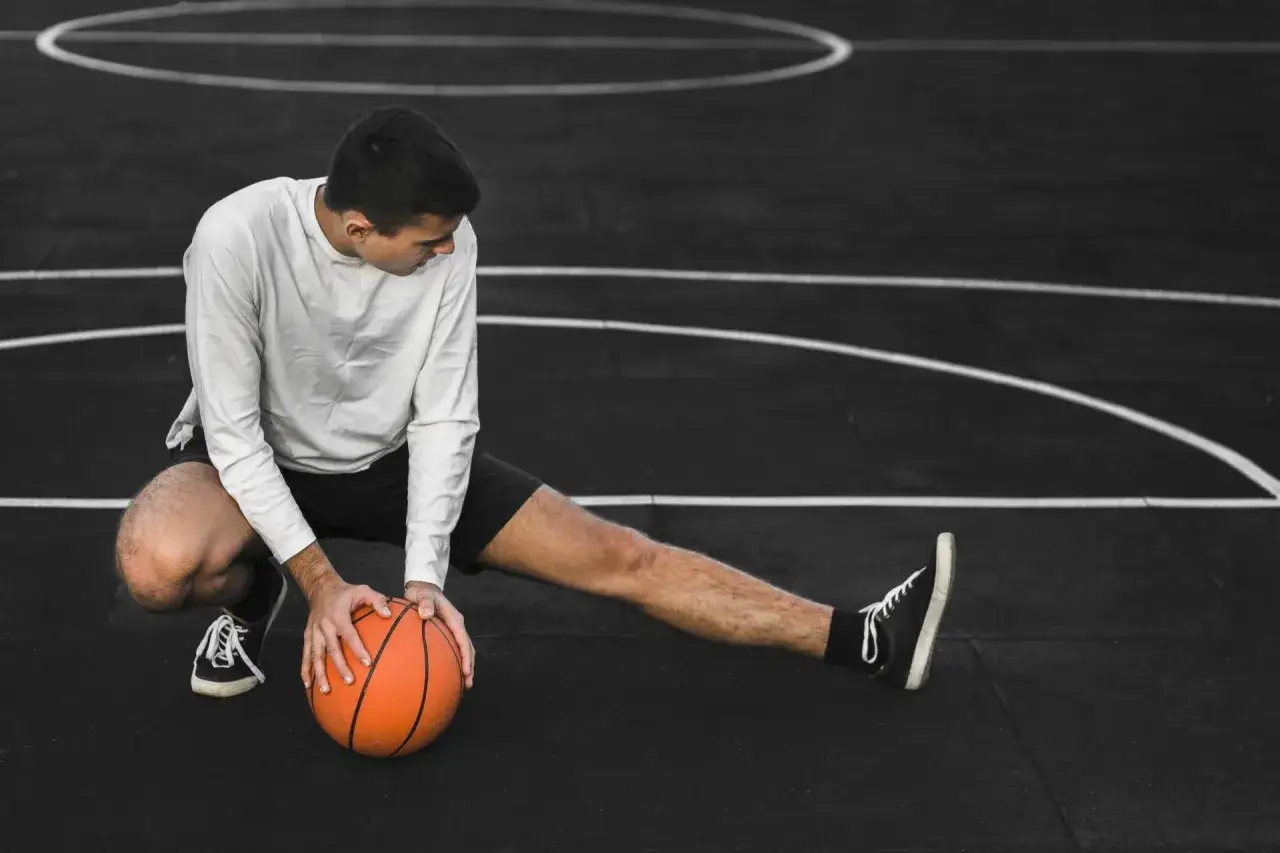 Giovane atleta si allunga sul campo da basket, pronto per il riposo muscolare di 48 ore.