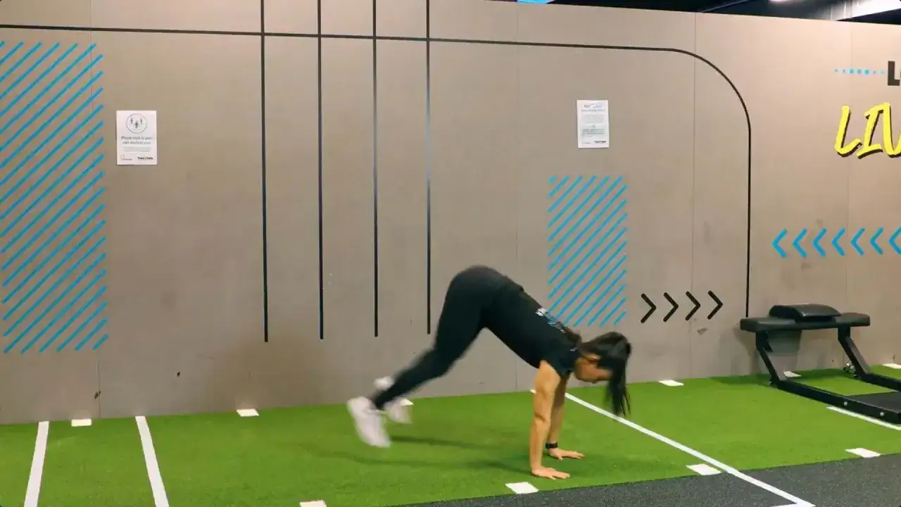 Donna esegue mezzi burpees in palestra, con un movimento dinamico e concentrato.