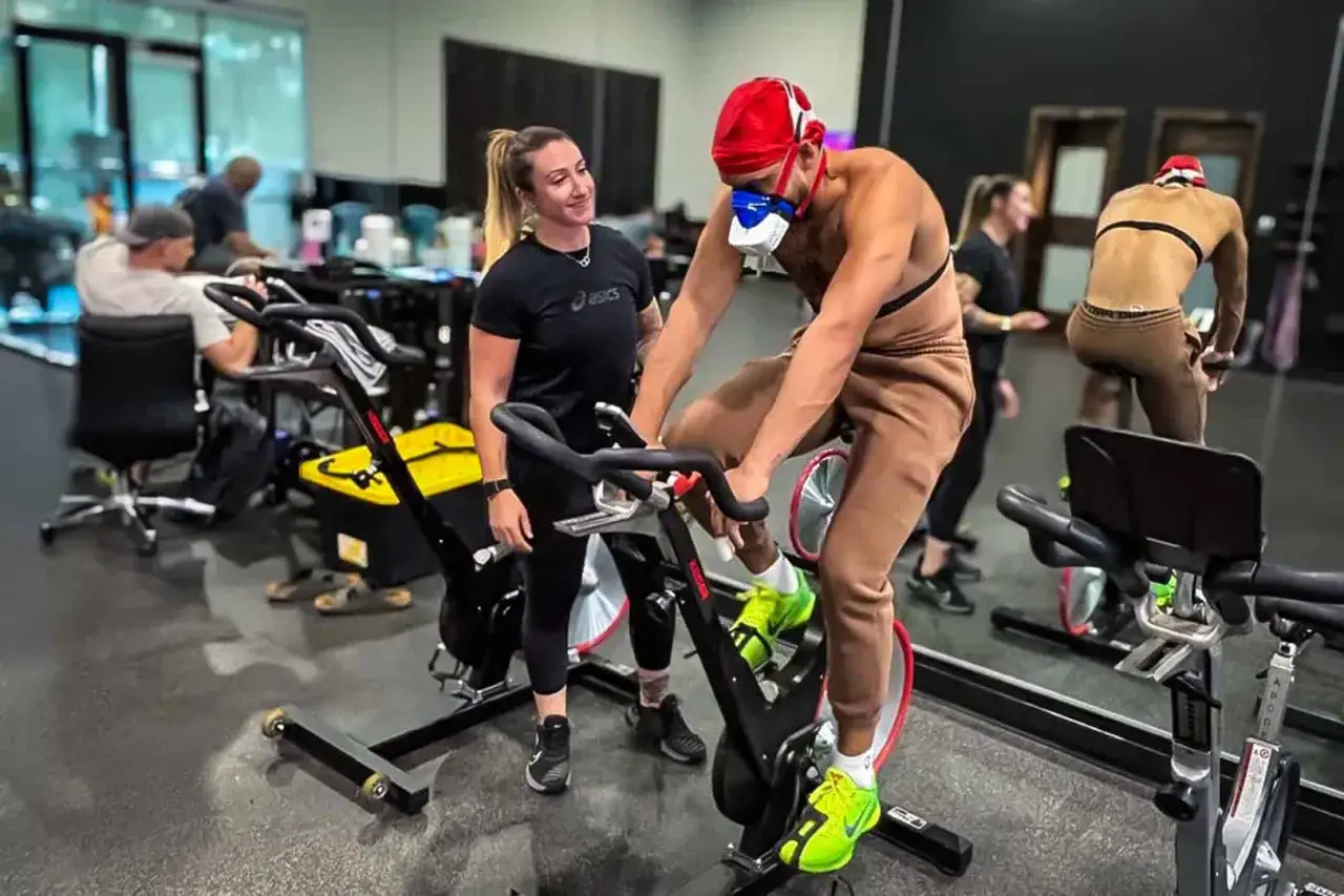 Allenamento intenso per misurare il VO2 max. Un atleta pedala con maschera e cardiofrequenzimetro, supervisionato da un'istruttrice.