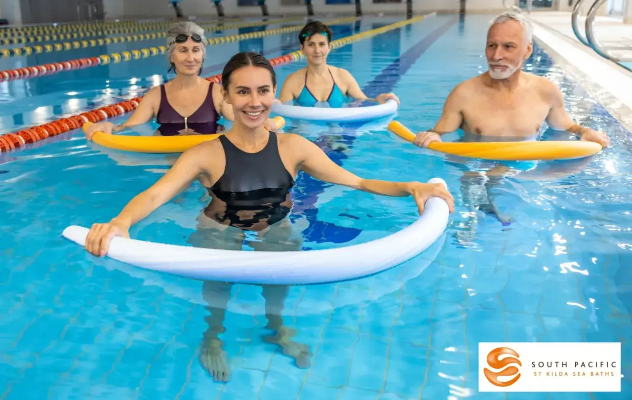 Persone di diverse et&agrave; fanno esercizi da fare in acqua al mare, usando galleggianti colorati per un allenamento divertente e salutare.