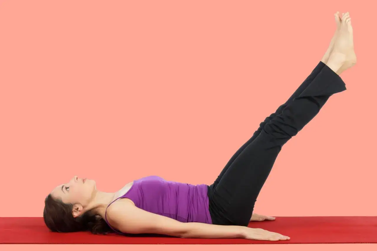 Donna con gambe in su, in posizione yoga su un tappetino rosso.