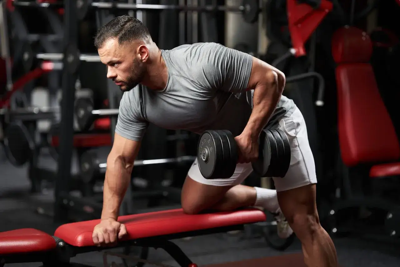 Uomo in palestra esegue rematore con manubrio, concentrato sui muscoli della schiena alta.