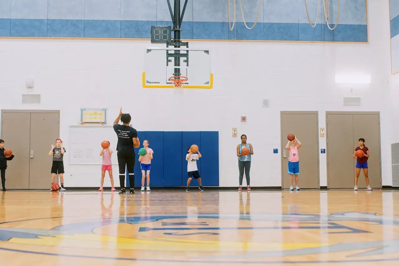 A group of children and adults practice basketball drills in a gym.