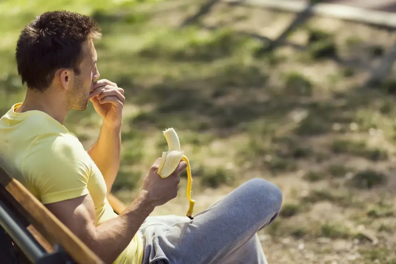 Uomo in panchina mangia una banana, perfetta banana prima o dopo allenamento per recuperare energie.